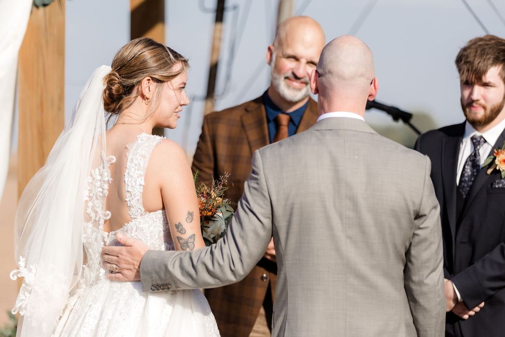 Wedding party gathers under a white tent for an outdoor celebration.