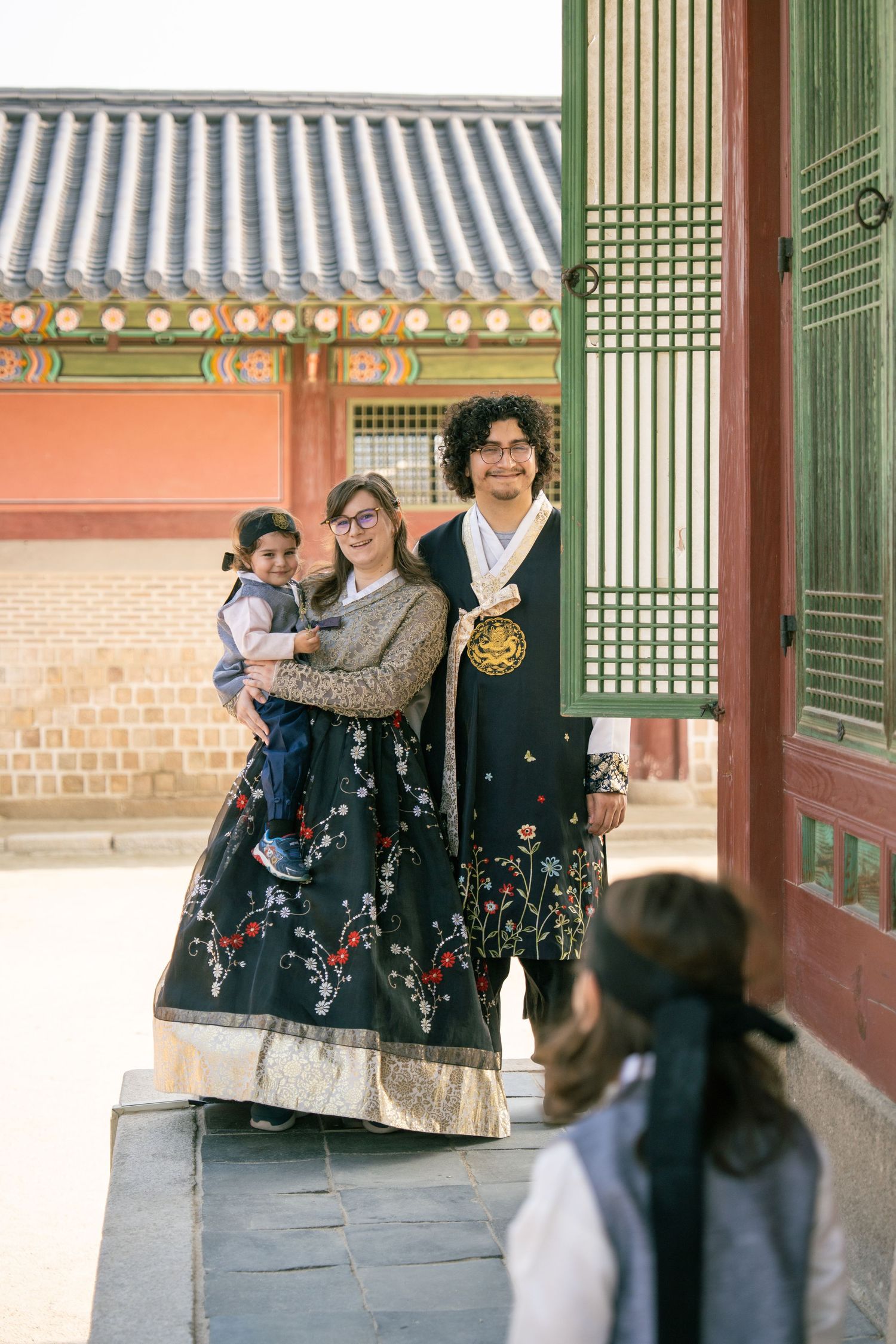 Visitors explore traditional Korean architecture with green wooden pillars and tiled roofs at a historic palace complex.