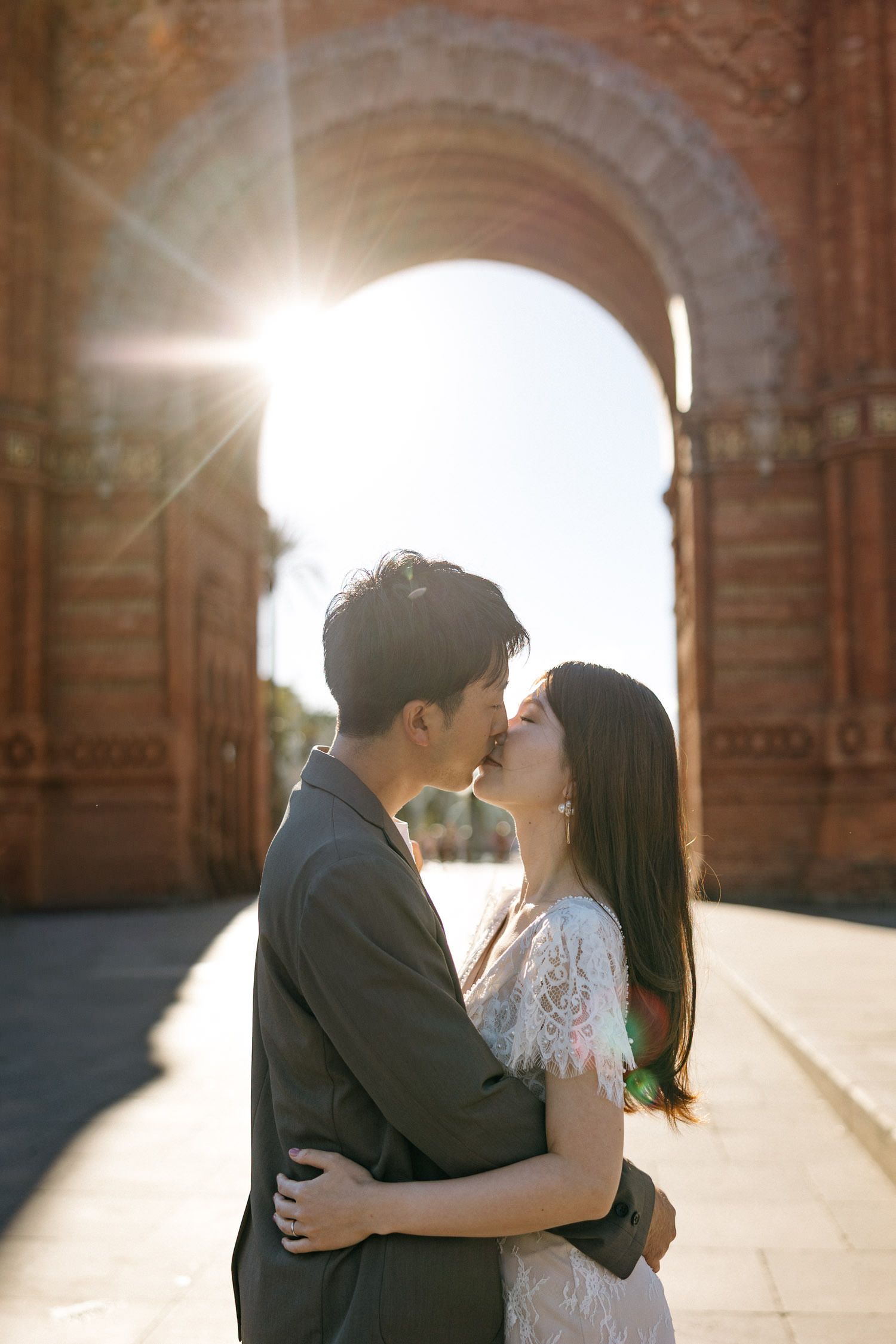 Couple embracing in sunlit stone archway creating romantic silhouette.