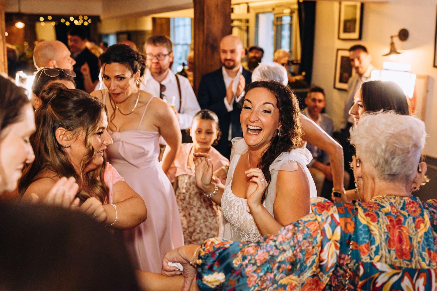 Wedding guests dance and celebrate together on a lively dance floor at an indoor reception venue.