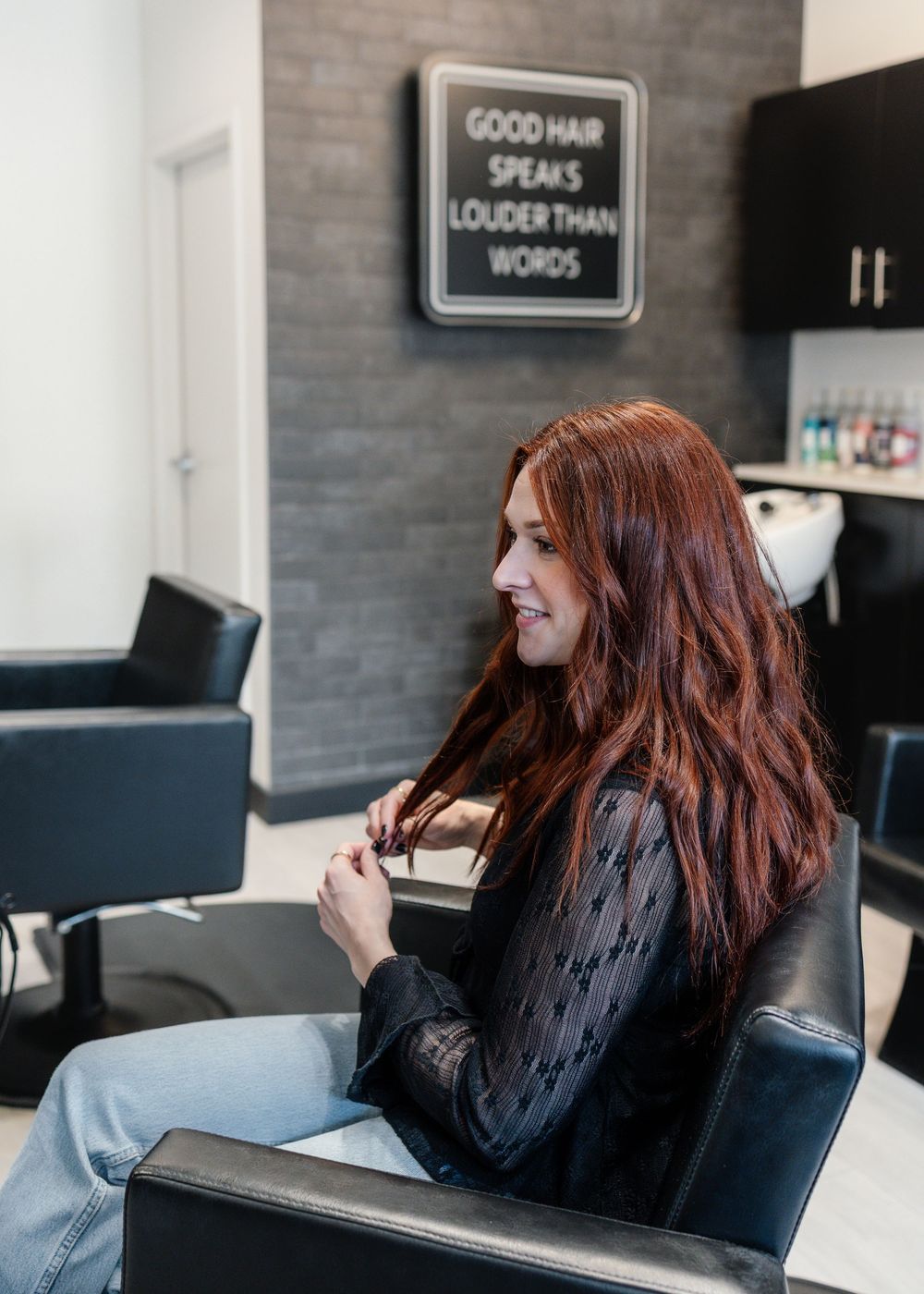 Red-haired woman sitting in a modern hair salon with motivational sign on wall.
