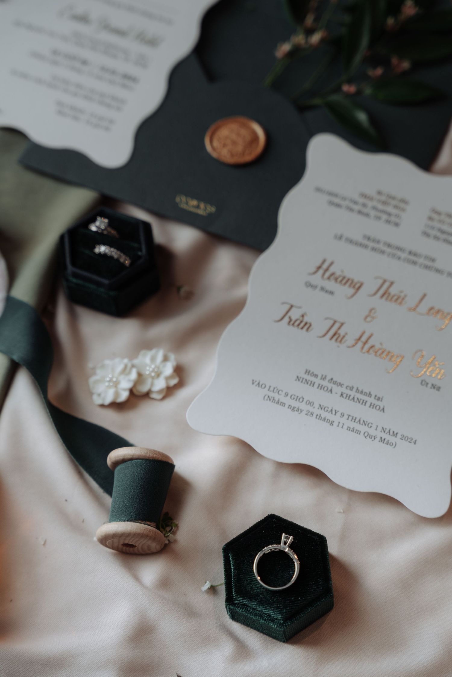 Wedding stationery flat lay with rings, green velvet boxes, and floral invitation cards.