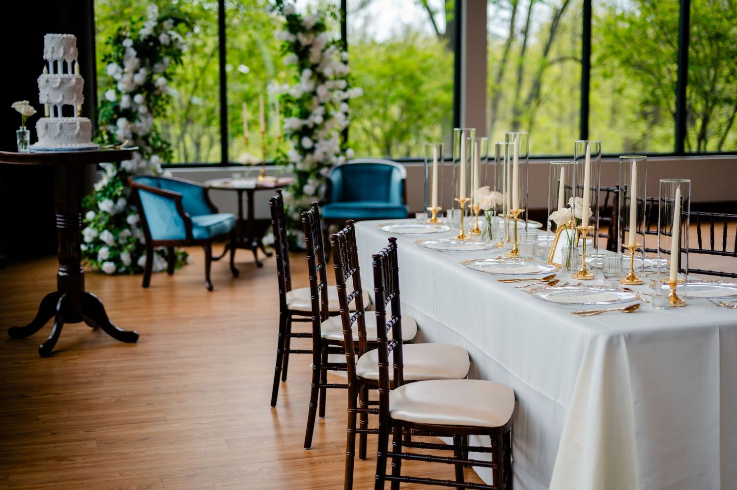 Elegant wedding reception tables set with white linens and gold accents in a rustic indoor venue with natural lighting.