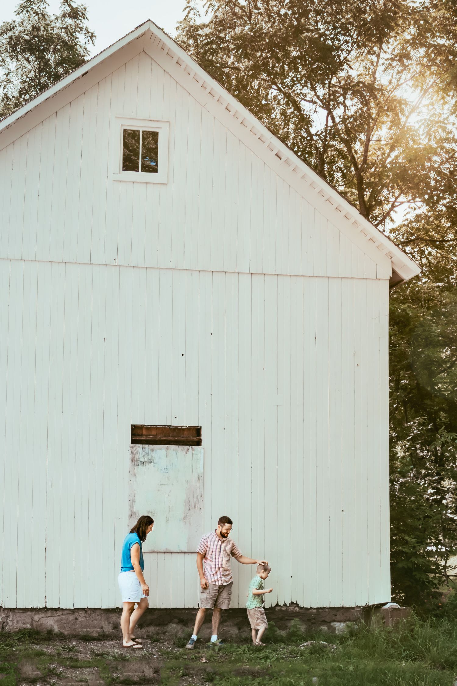 A series of four photos showing people playing hide and seek around a white barn building at sunset.