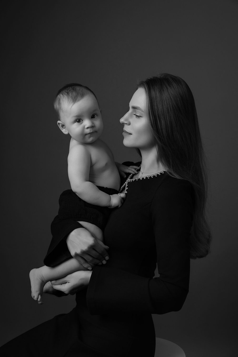 Black and white portrait series showing tender moments between a parent and baby in dramatic lighting.