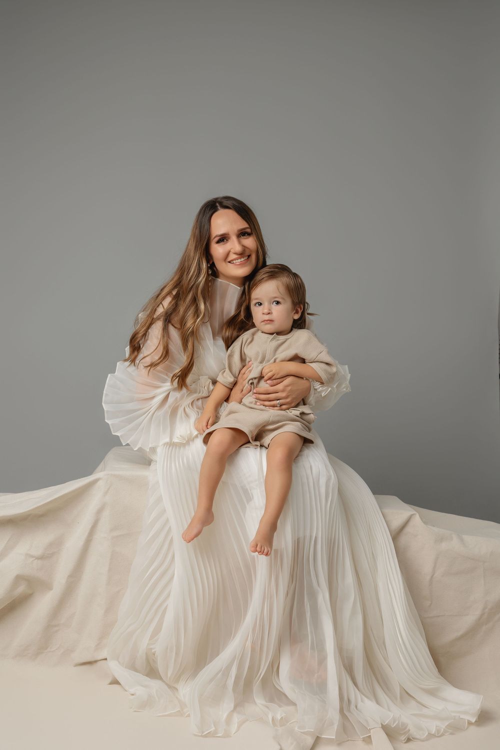 A series of tender studio portraits showing a mother and child in flowing white dresses against a neutral gray backdrop.