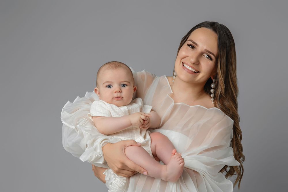 A baby in a white christening gown is held lovingly while being photographed in a series of tender moments.