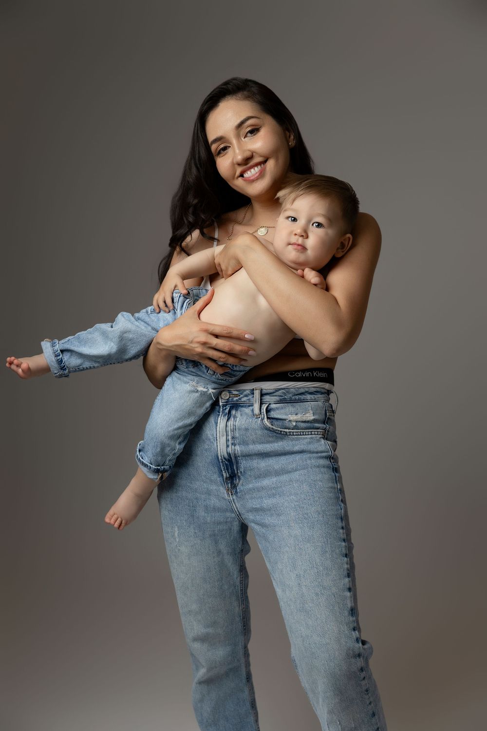 A series of four candid photos showing a parent and baby in casual denim jeans against a grey studio backdrop.