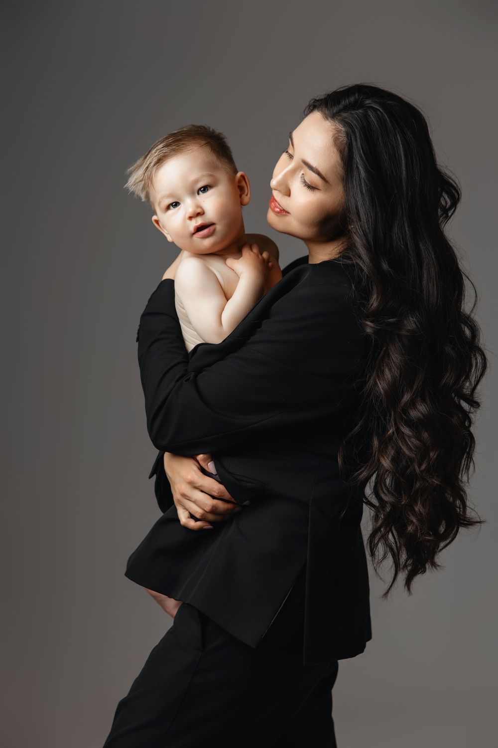 A series of artistic black and white studio portraits showing tender moments between a parent and child against gray backdrop.