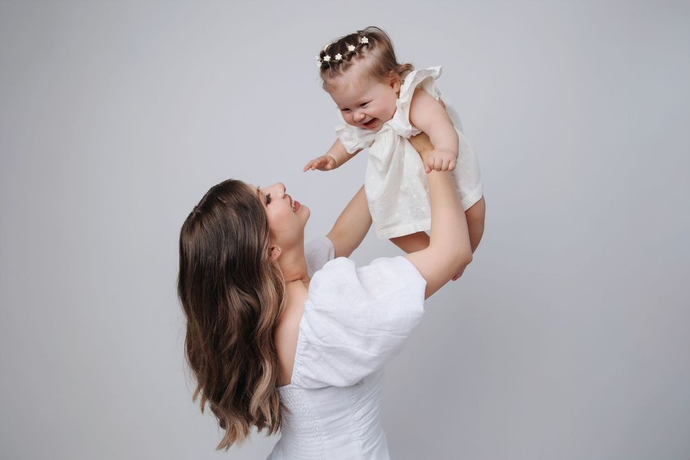 A mother in white holds and lifts a baby in a series of joyful, playful poses against a light background.