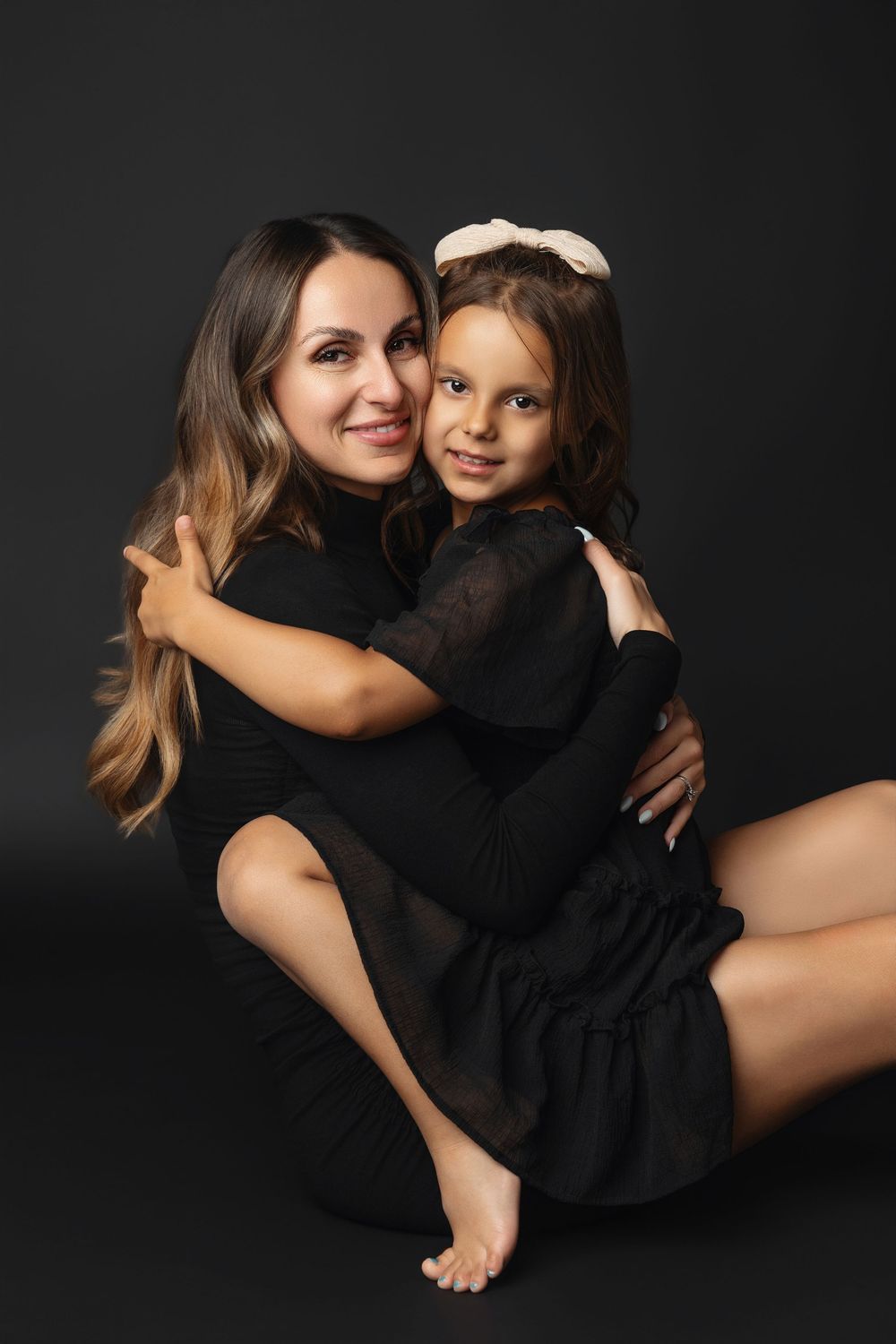 A series of intimate black and white portraits showing tender moments between a parent and child against dark background.