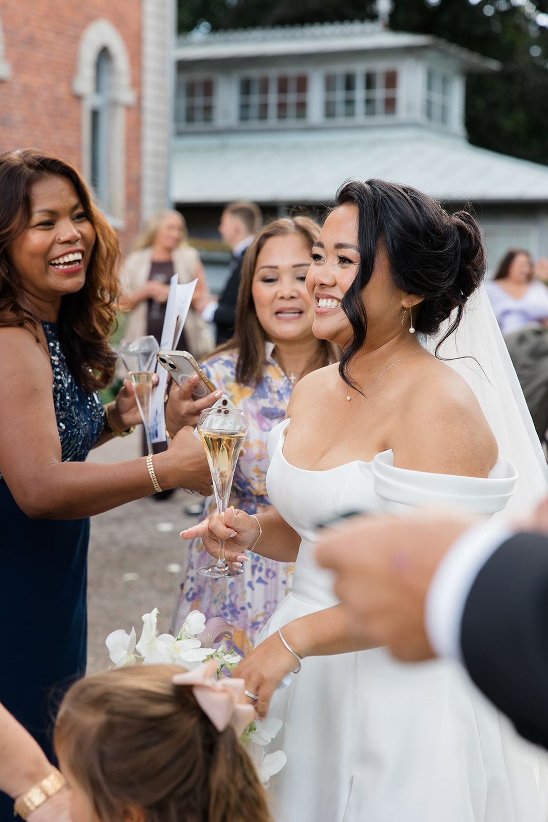 A joyful wedding celebration scene with guests and the bride sharing champagne toasts outdoors.
