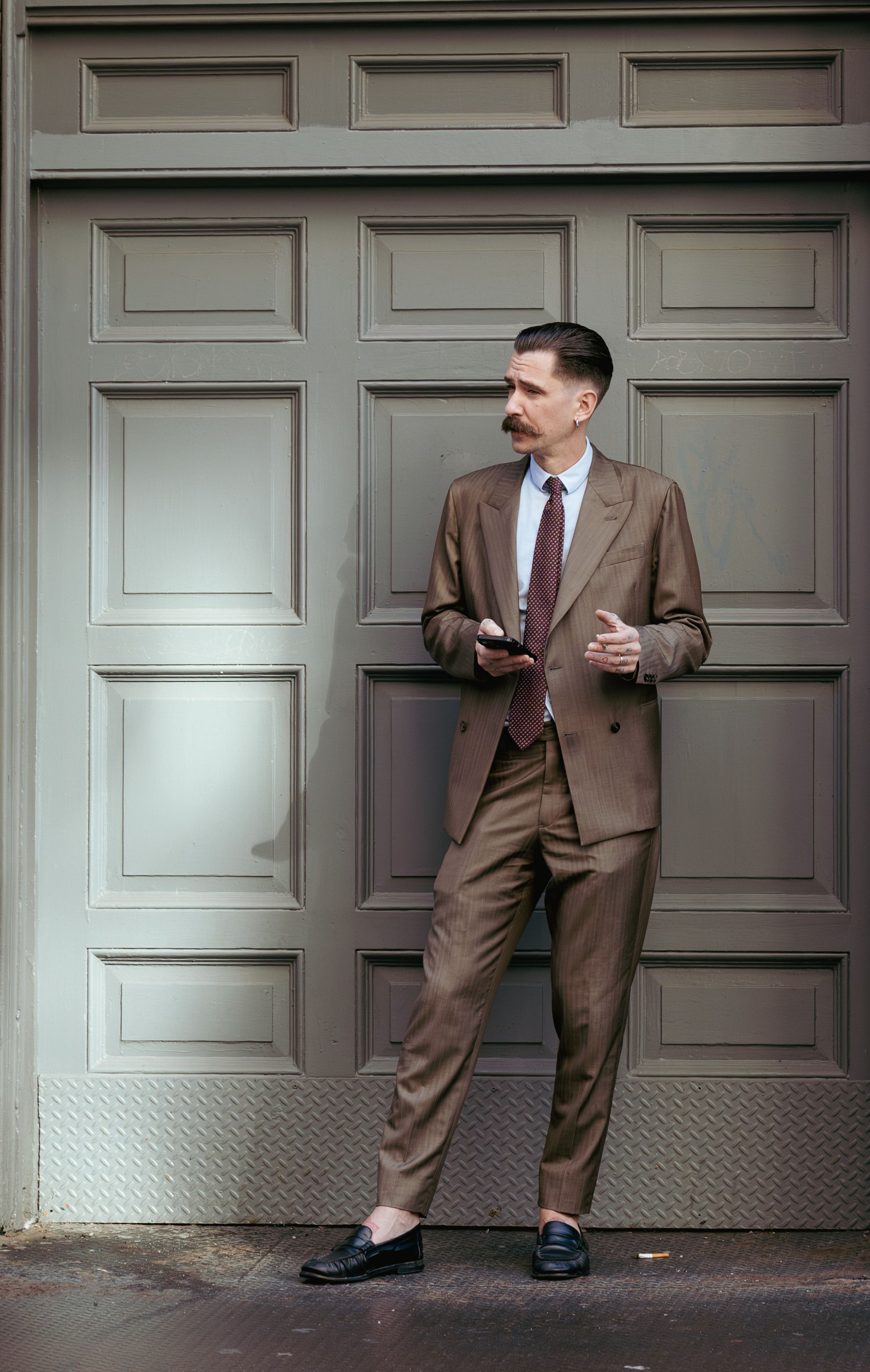 A person in a brown suit poses playfully in front of a gray door in a sequence of four connected images.