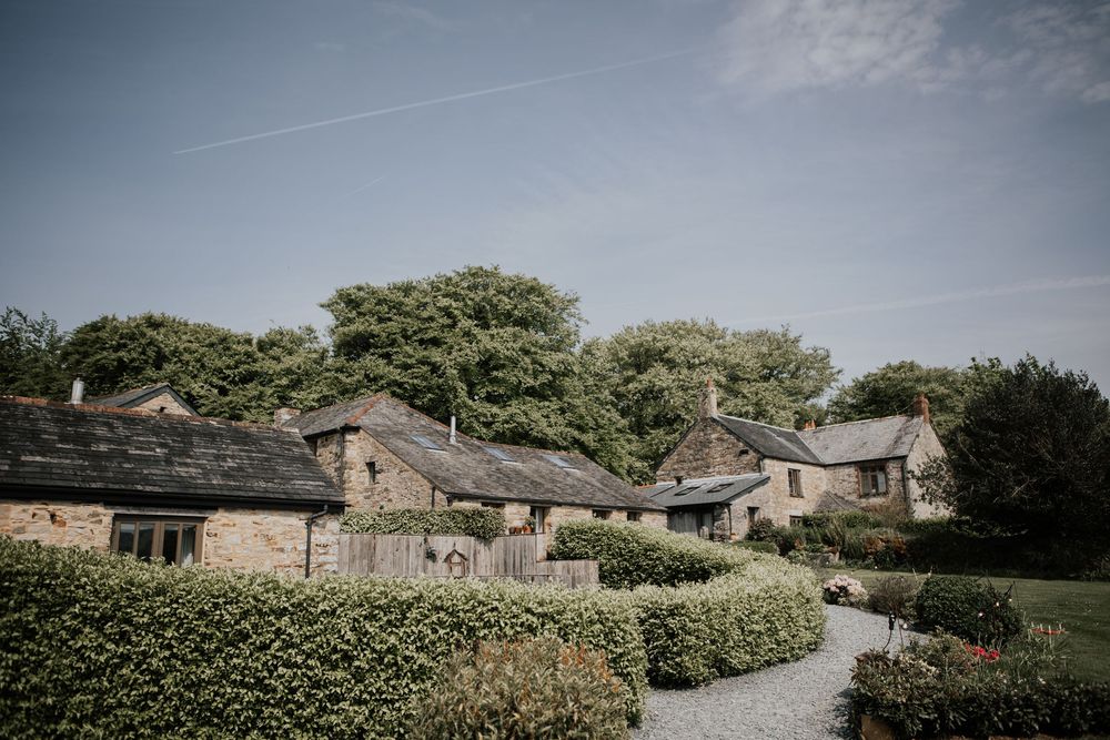 Beautiful countryside stone cottage wedding venue with lush green hedges and gravel path on a sunny day.