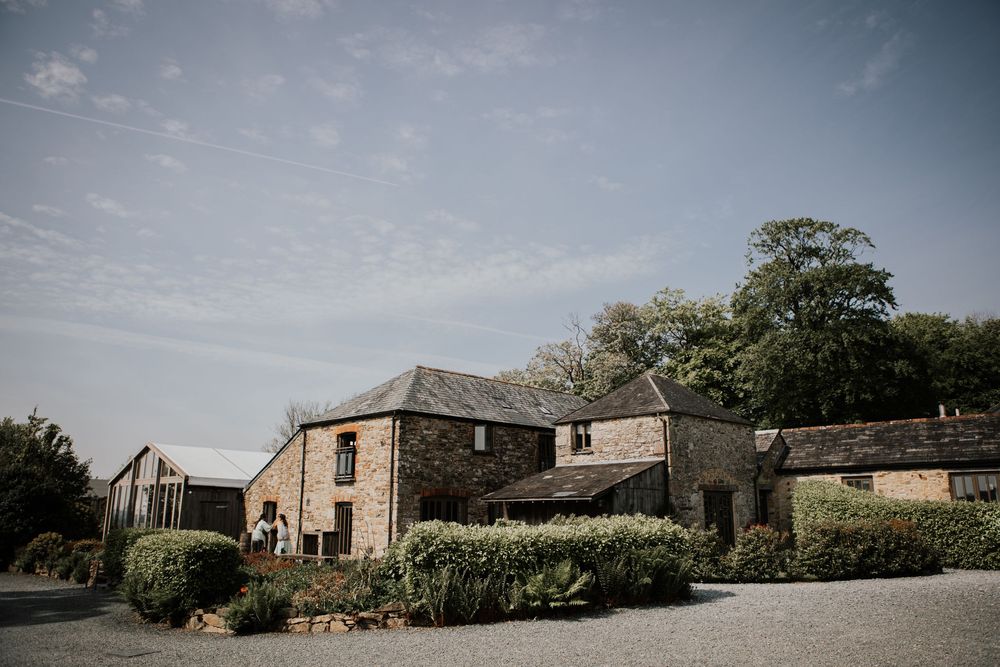 Charming rustic stone farmhouse wedding venue surrounded by trees under a clear blue sky.