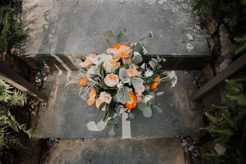 Elegant bridal bouquet of peach roses and eucalyptus greenery placed on stone steps for a wedding.