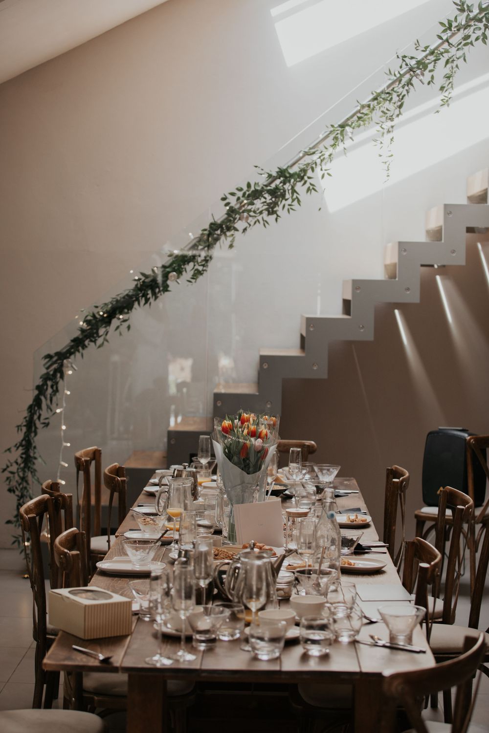 Beautifully set wedding reception table with greenery garland along staircase railing and tulip centerpiece.