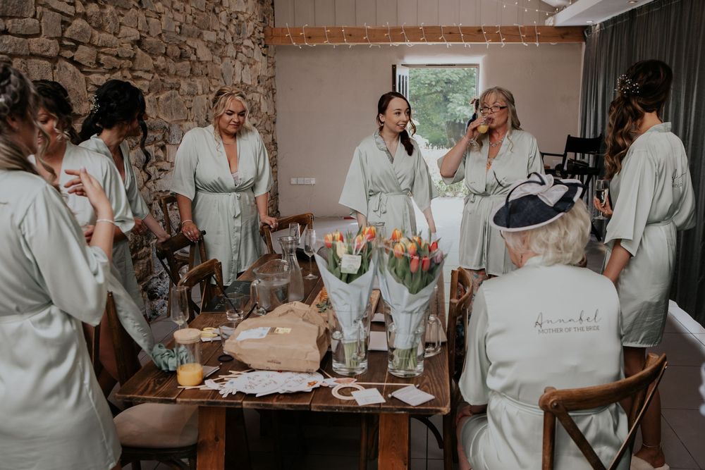 Bridal party in matching sage green robes gathered around a table with tulips during wedding morning preparations.