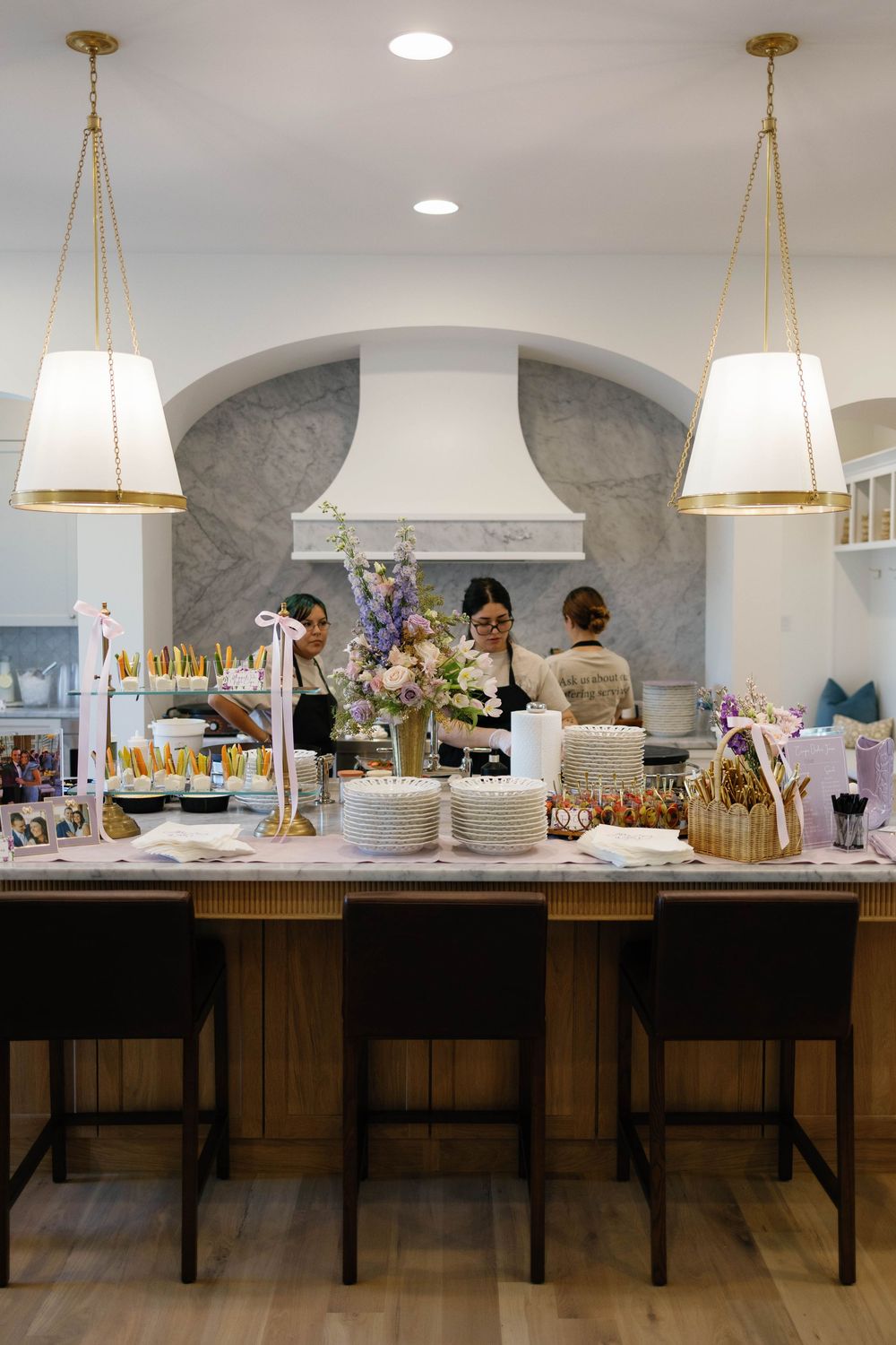 Bright white kitchen with pendant lights, marble hood, and a floral centerpiece on a large island for a bridal shower.
