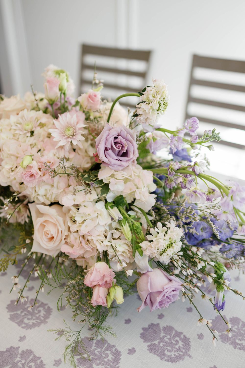 Elegant floral centerpiece with pastel pink and purple roses on a patterned tablecloth.