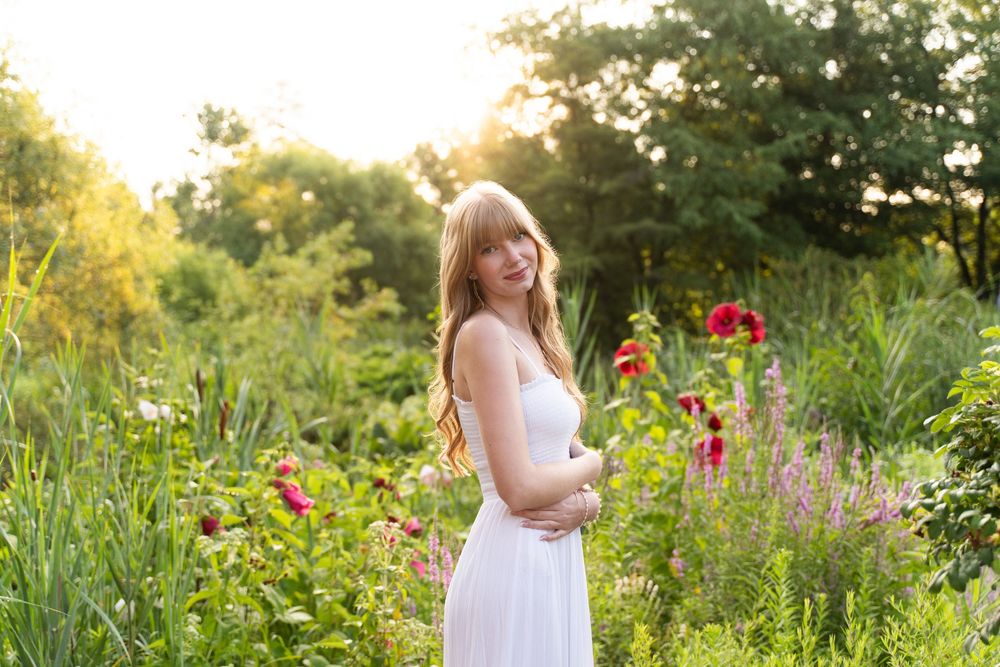 A Perrysburg High School senior in a white dress stands among vibrant wildflowers during golden hour in a summer garden.
