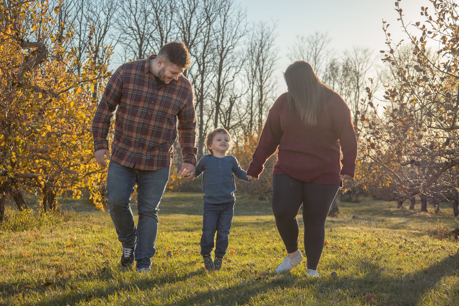 Family walking together in a golden autumn field at sunset casting long shadows on the grass.