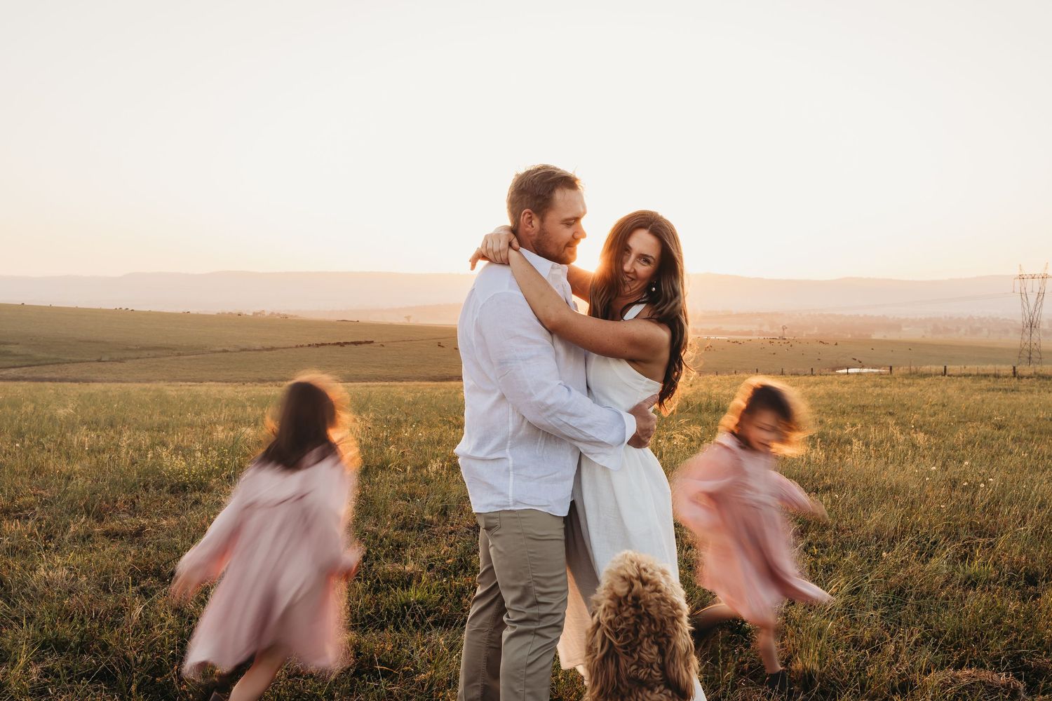 Couple dancing together in a golden field at sunset while her pink dress flows in the wind.
