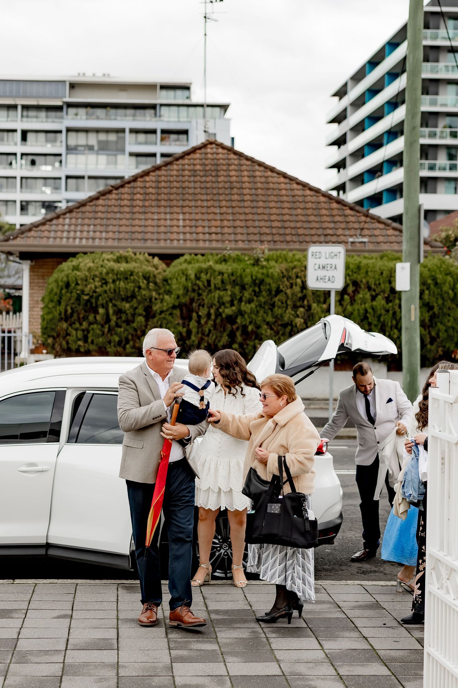 Outdoor gathering of guests on a paved terrace with apartment buildings in the background.