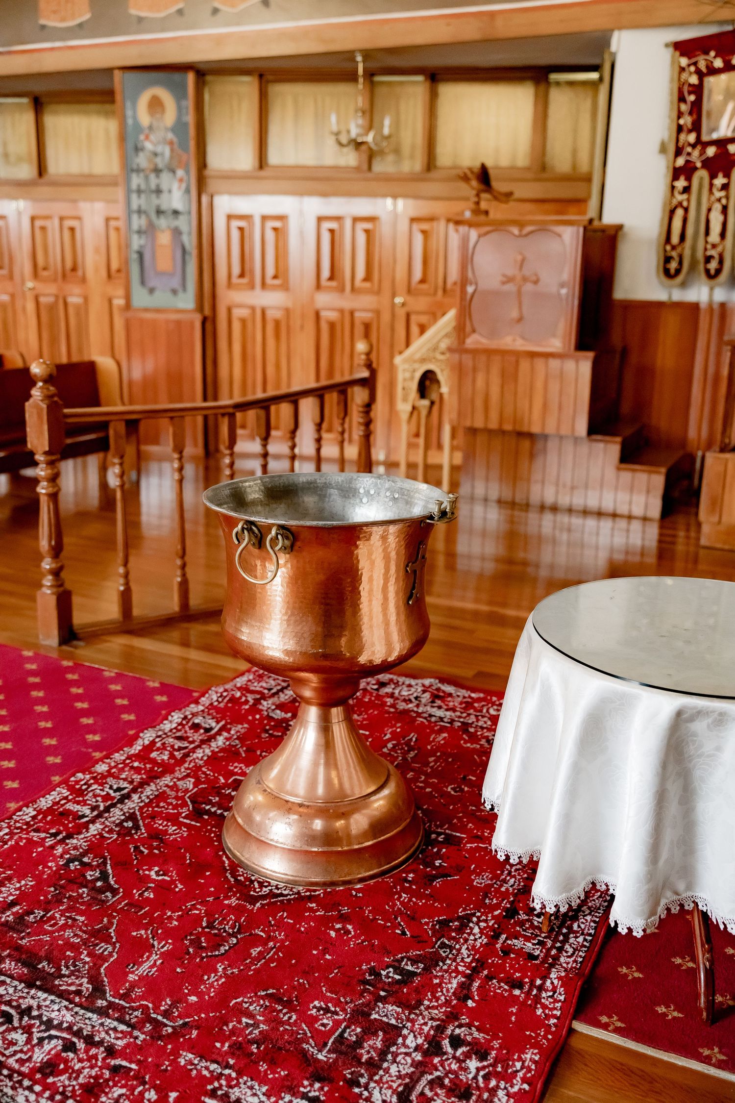 Church interior with ornate copper baptismal font on red carpet and wooden paneled walls.