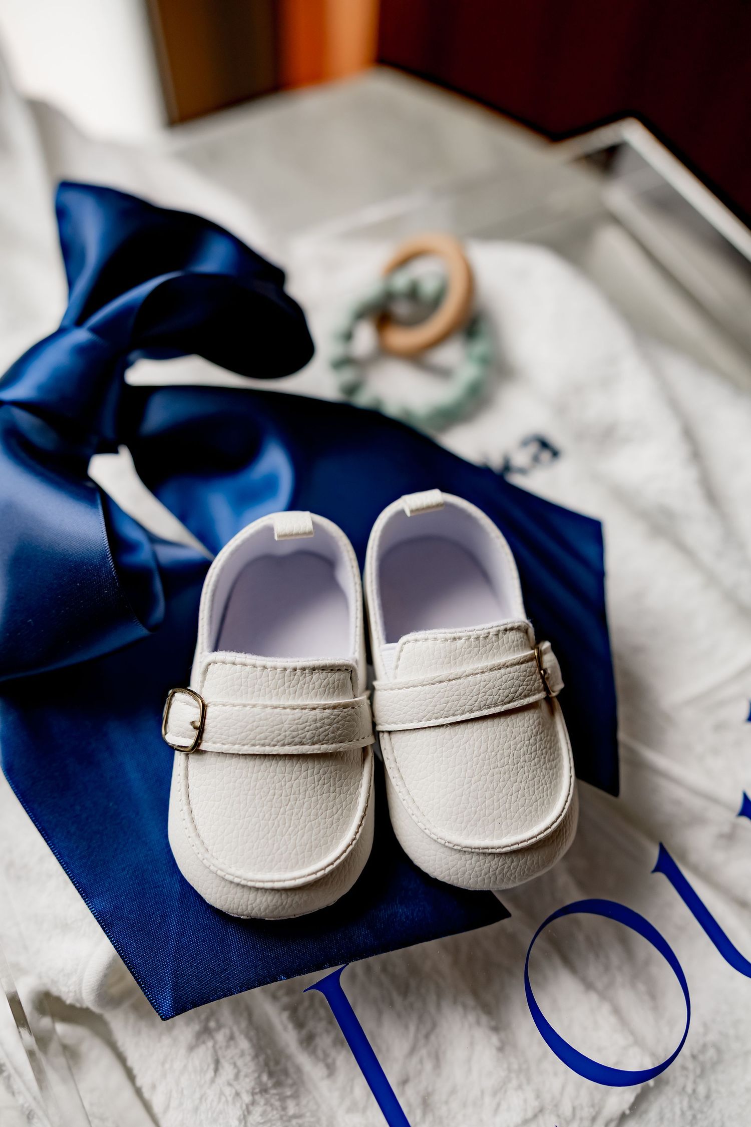 Small white baby dress shoes placed on navy blue ribbon against white fabric.