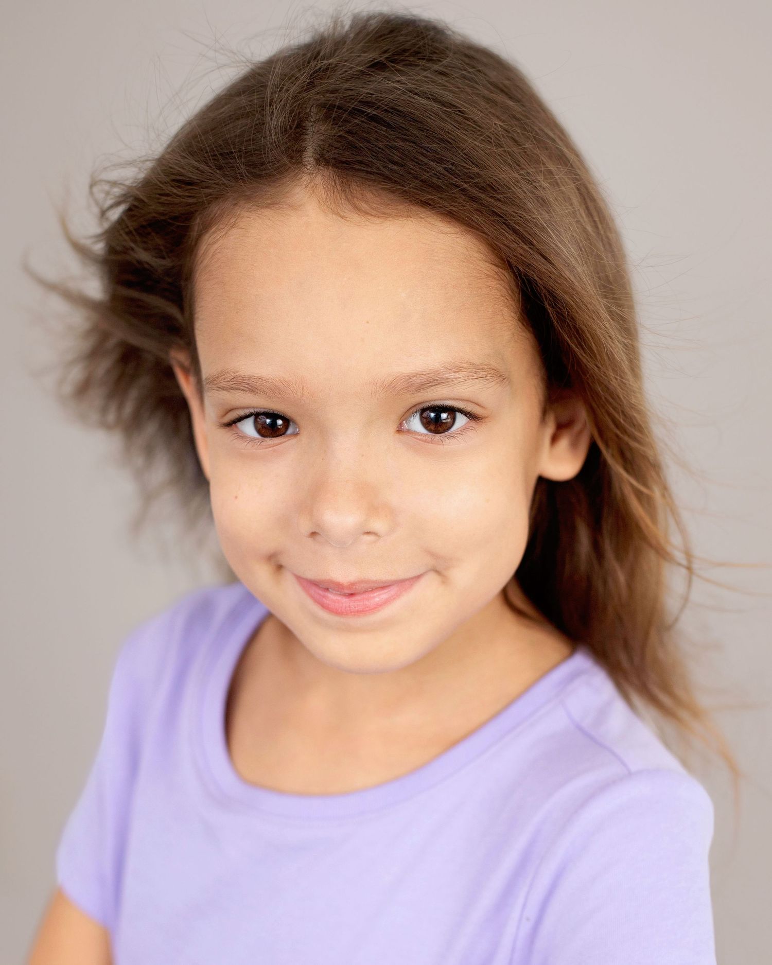 A child in a lavender shirt smiles playfully in a series of expressive portrait poses against a neutral background.