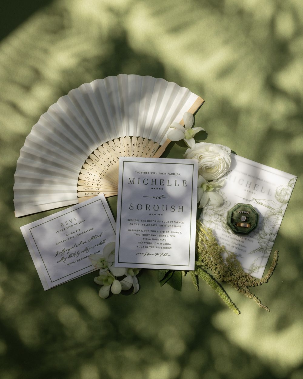 Wedding invitation suite with white paper fan and floral elements in natural lighting.