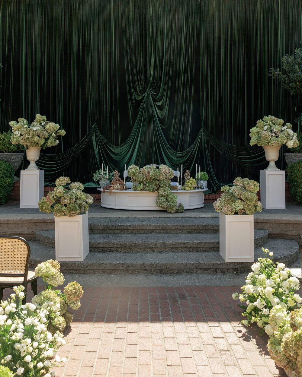 Wedding venue stage decorated with dark green curtains and white floral arrangements.