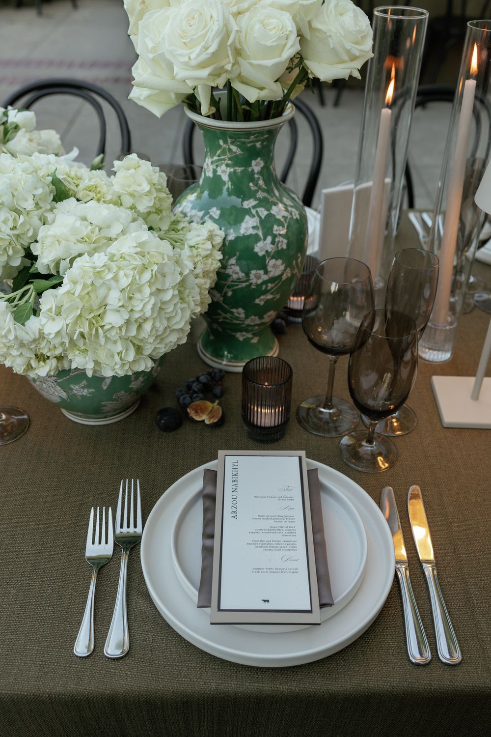 Elegant table setting with white hydrangeas, glass vases, and place settings on gray linen.