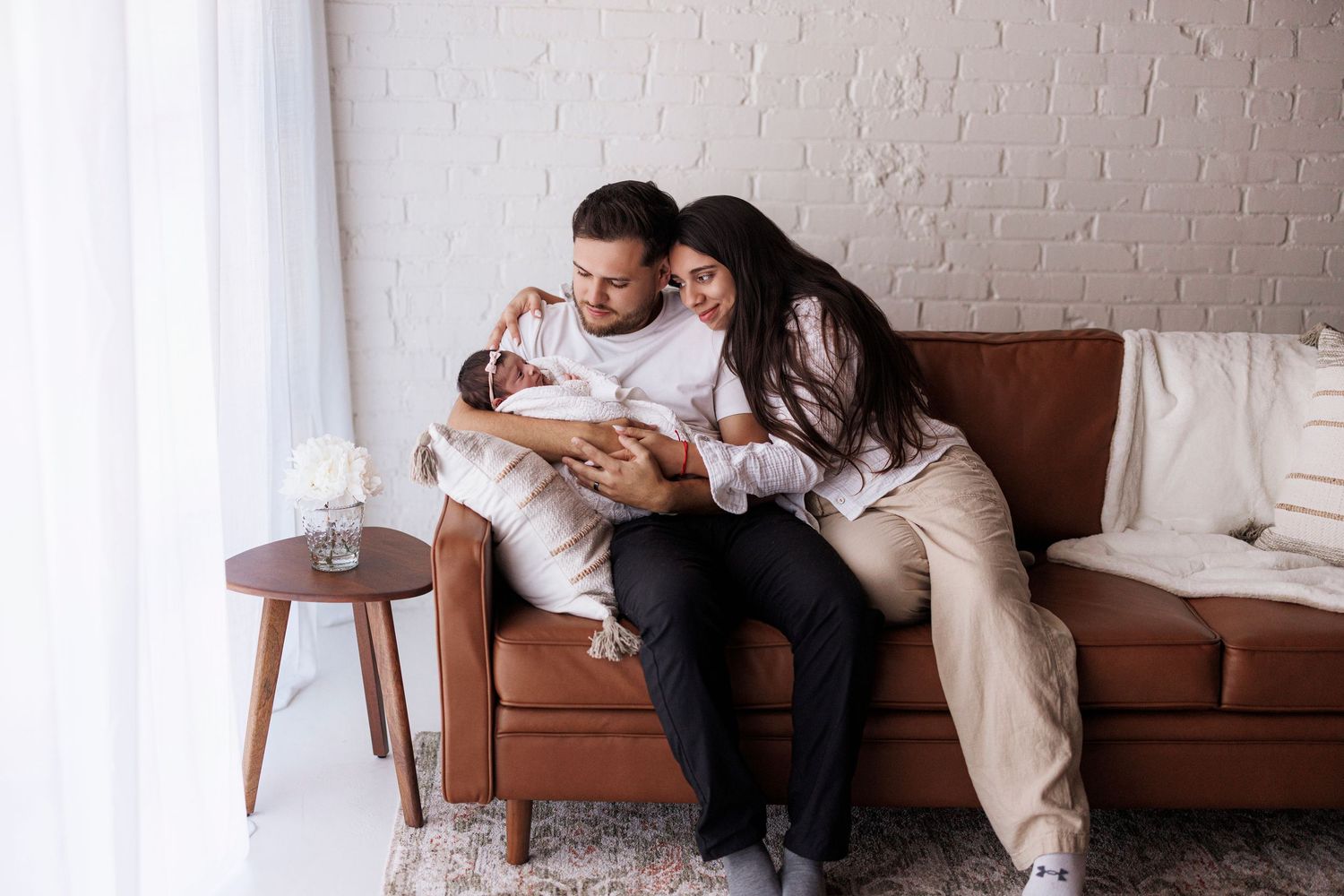 A couple embraces on a brown leather couch in a minimalist room with white walls.