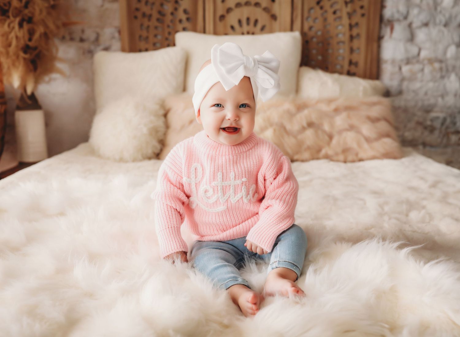 Baby wearing grey sweater smiling and playing on white bedding.