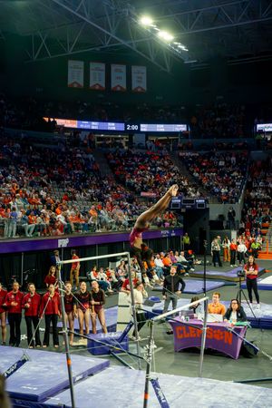 A sequence of gymnasts performing routines on the uneven bars during a collegiate gymnastics competition.