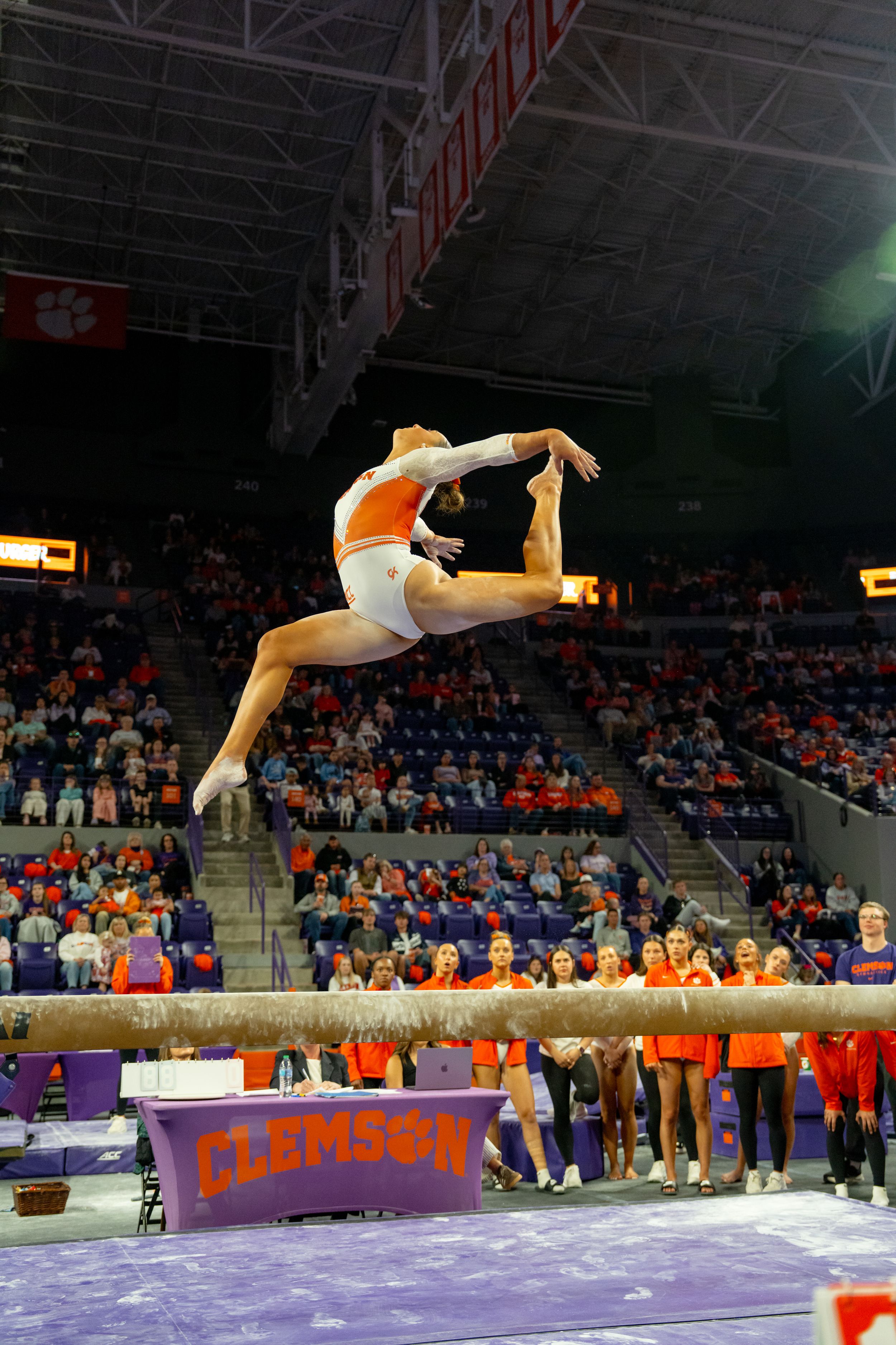 Clemson gymnast performs a stunning leap on the balance beam during a collegiate gymnastics meet at Clemson University arena.