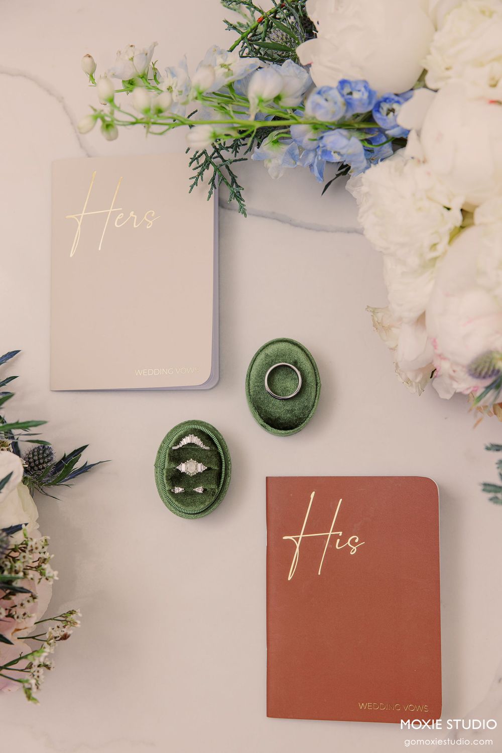 Elegant wedding stationery set with terracotta cards and green bottles surrounded by delicate white and blue flowers.