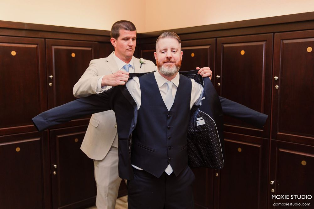 People in formal attire walk through an elegant wood-paneled hallway with ornate lighting fixtures.