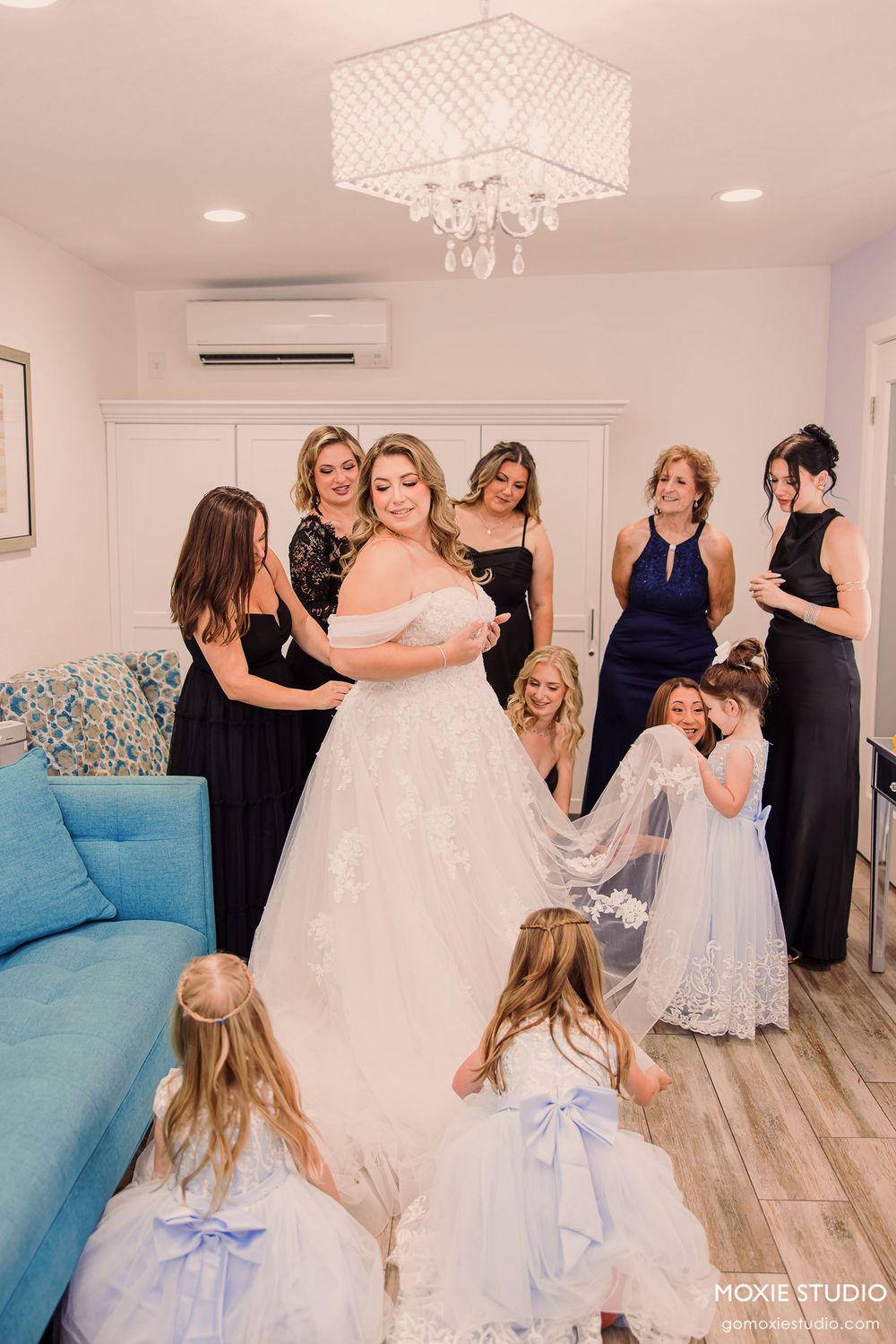 A series of photos showing bridesmaids in navy dresses helping the bride with her white wedding gown in a bright room.