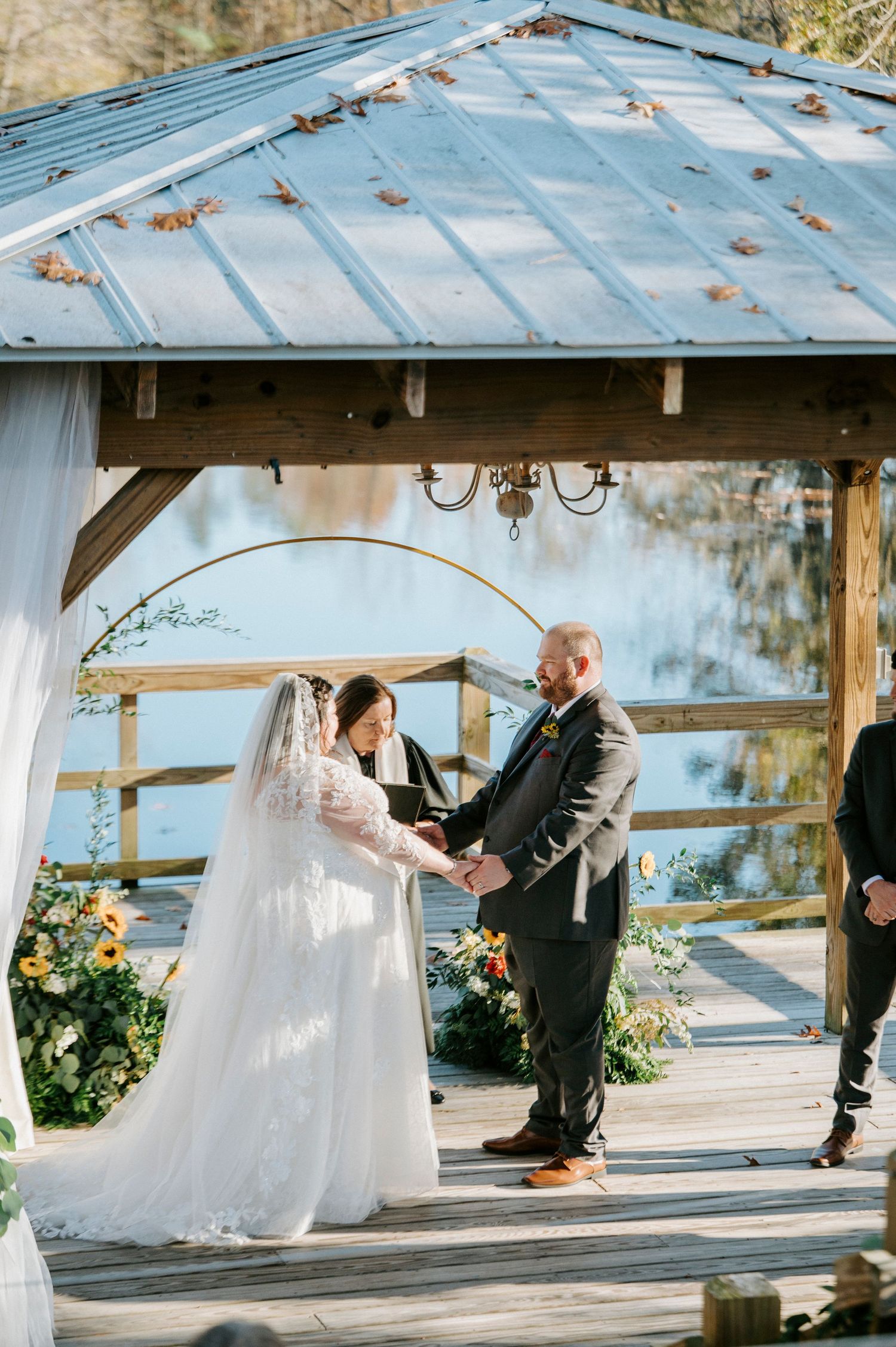 A couple shares a romantic dance moment under a rustic wooden gazebo with blue water views in the background.