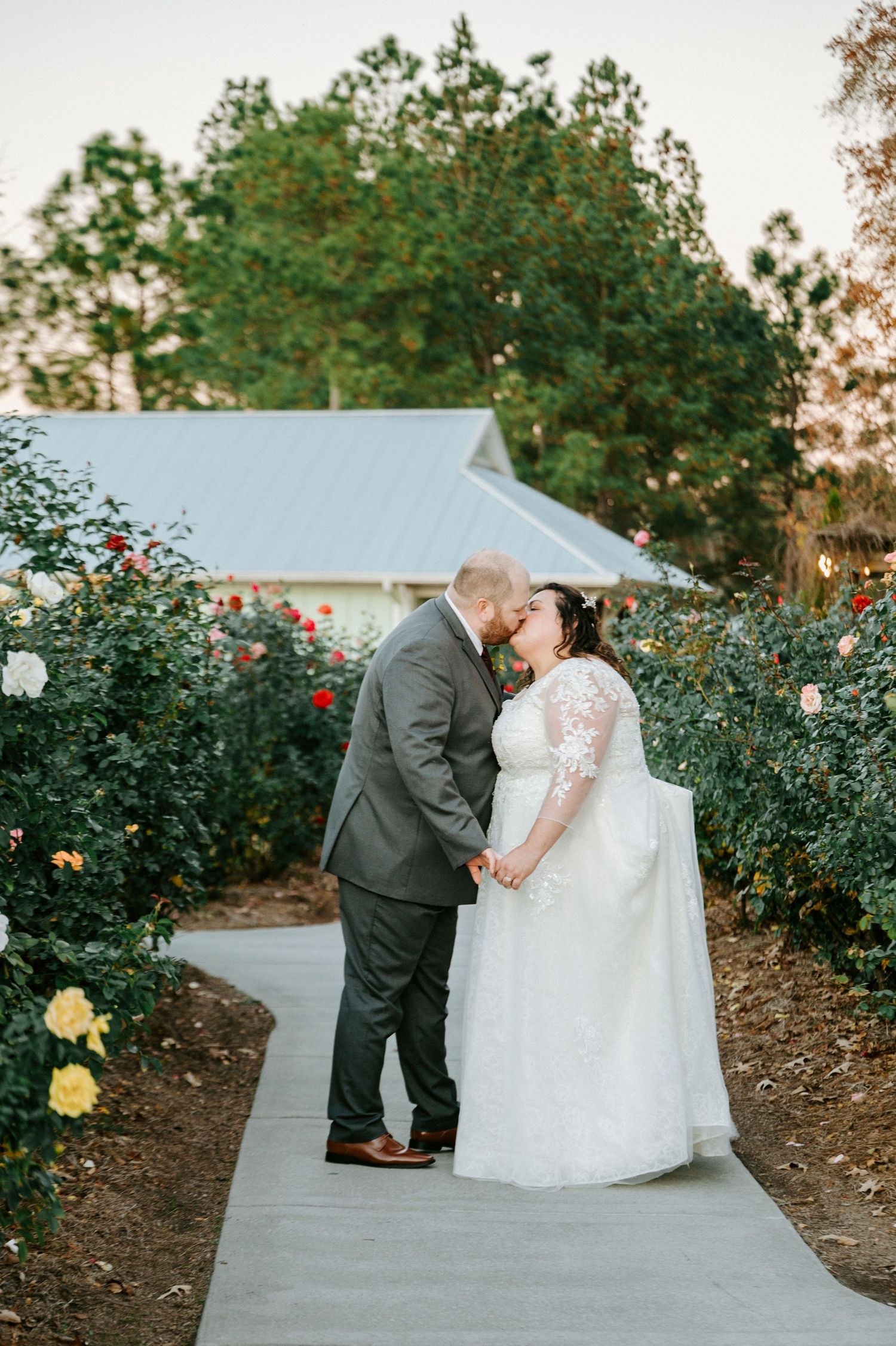 A romantic wedding couple shares intimate moments in a garden with blooming roses at sunset.