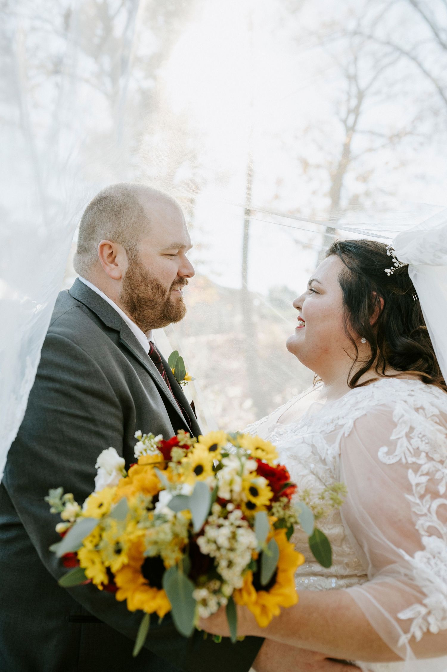 A couple shares a romantic moment at their winter wedding with a vibrant sunflower bouquet and lace dress details.