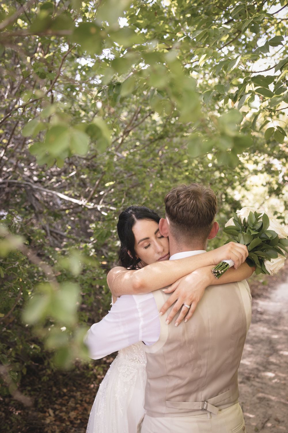 A couple embraces in a romantic outdoor setting surrounded by green foliage and natural light.