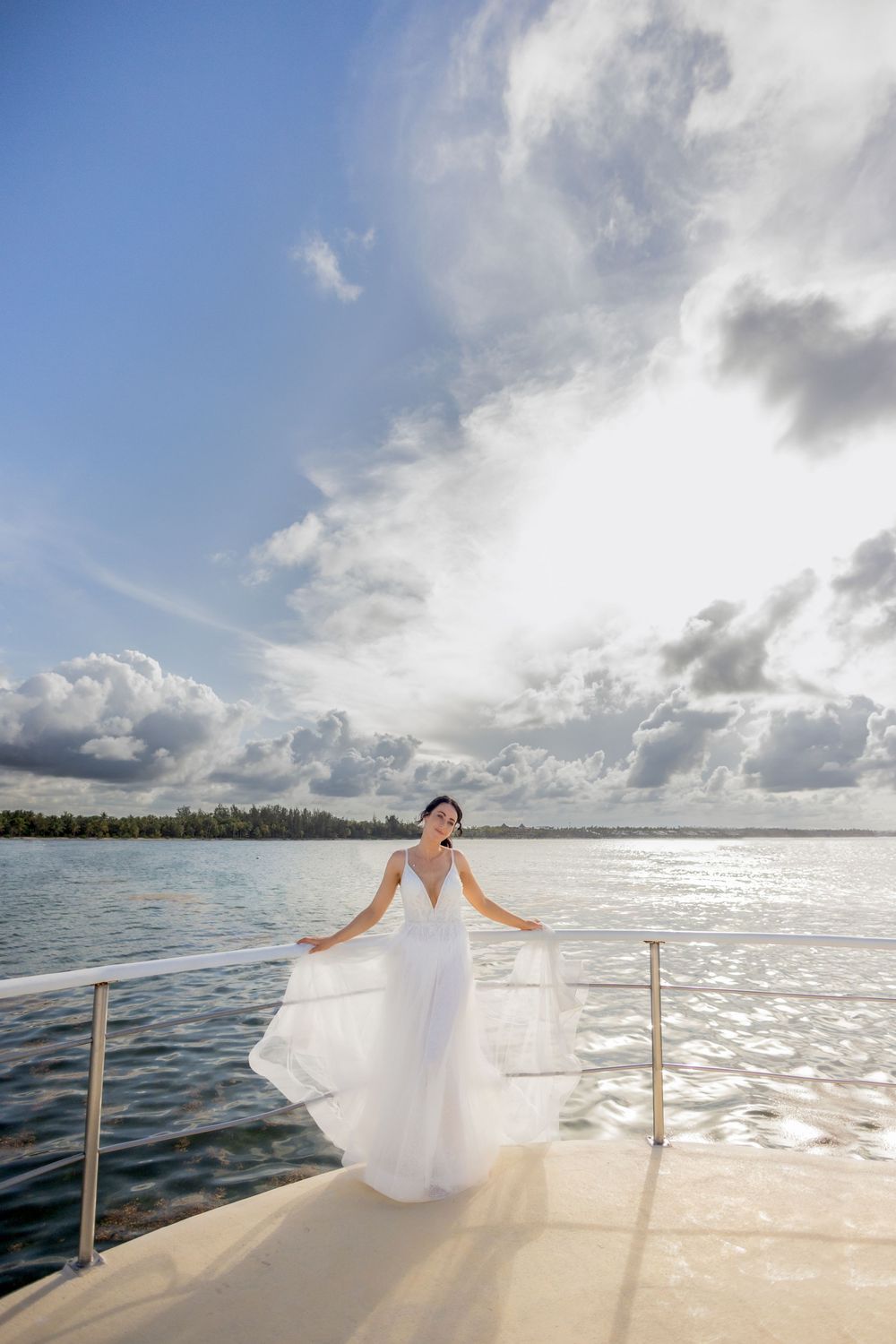 White wedding dress flowing in the breeze on a boat deck against a dramatic cloudy ocean backdrop.
