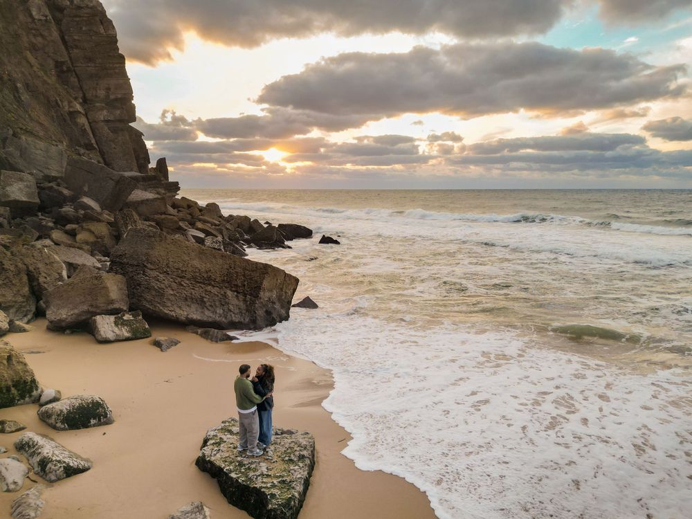 Dramatic coastal landscape with rocky cliffs and sandy beach at sunset as waves crash against the shore.