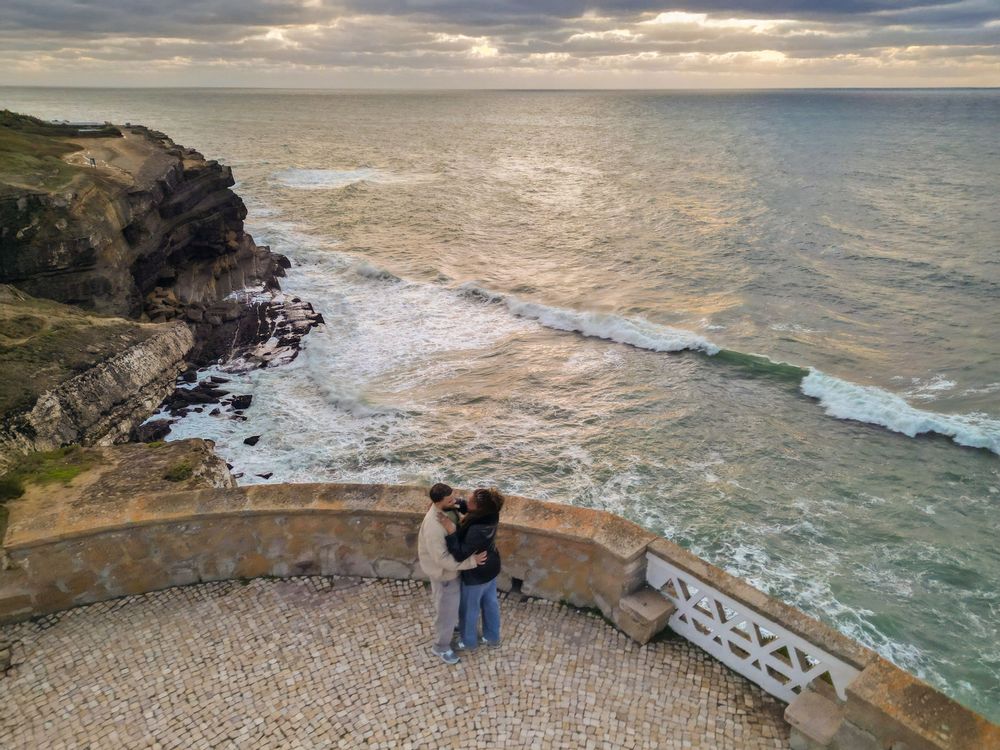 Scenic coastal viewpoint overlooking rocky cliffs and crashing waves at sunset with stone viewing platform.