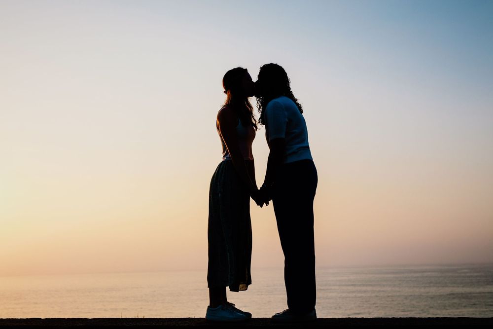 Two silhouettes embrace on a beach at sunset with ocean waves in the background.