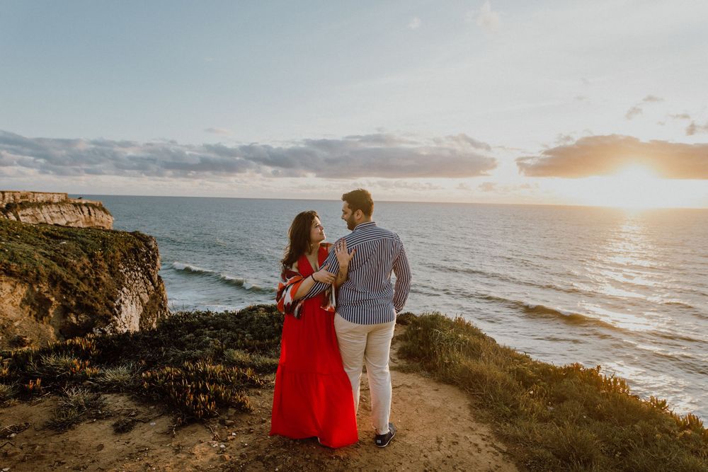 Scenic coastal engagement photos at sunset with waves crashing against cliffs in the background.